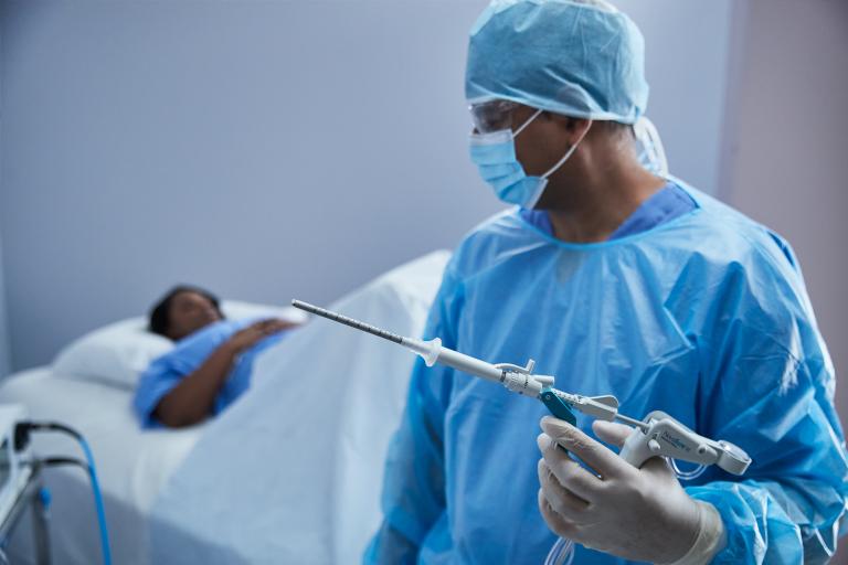 Chirurgien en blouse tenant un dispositif médical avec une patiente allongée sur un lit d’hôpital