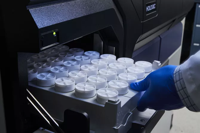 Gros plan d’une main gantée insérant un plateau de tubes médicaux dans un dispositif