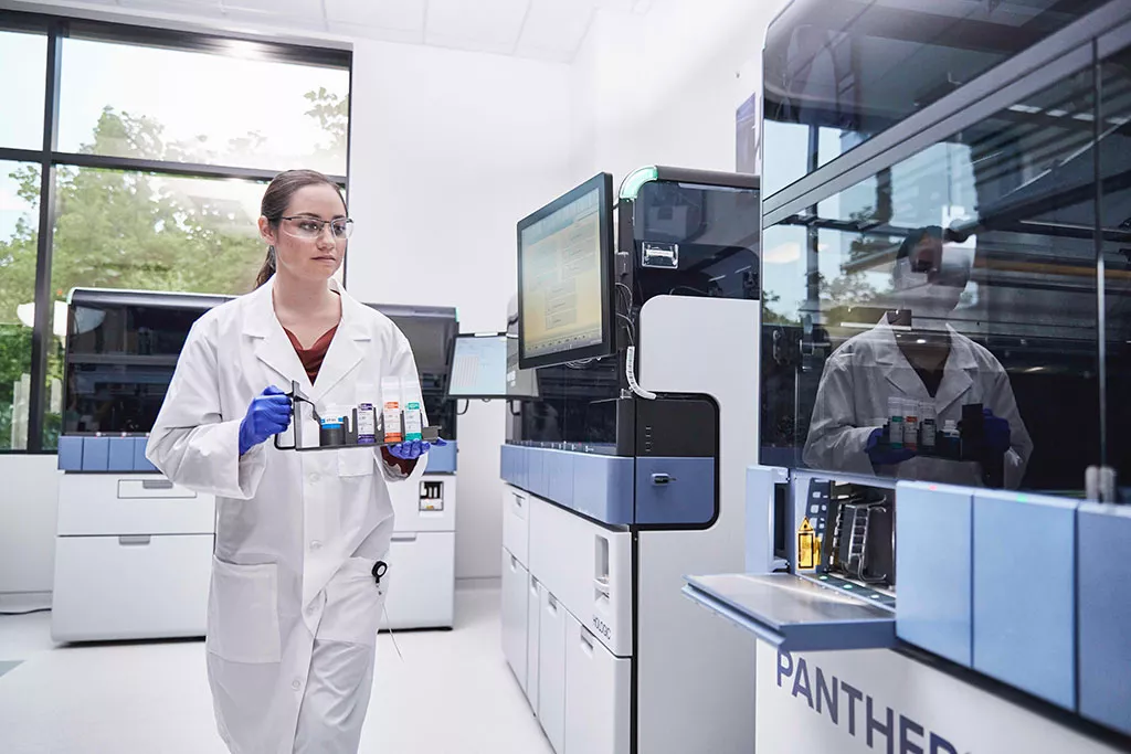 Technicienne de laboratoire transportant un plateau d’échantillons à insérer dans le système Panther