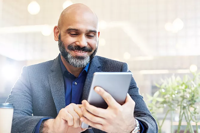 Un homme sourit en regardant une tablette à l’extérieur