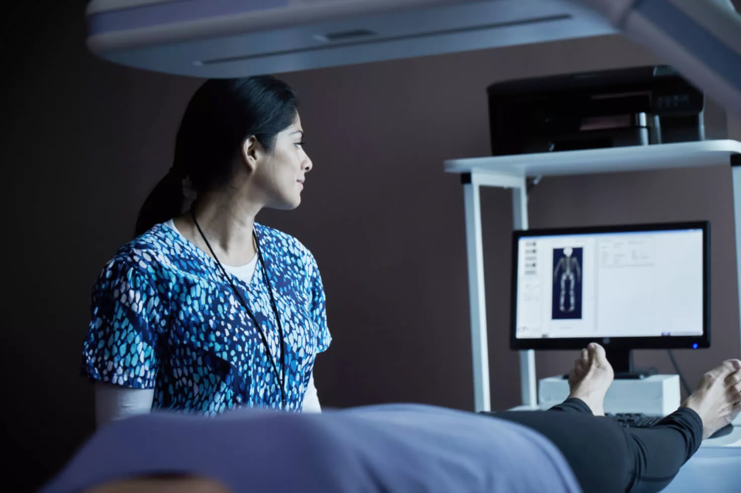 Professionnelle de santé regardant un scanner sur un écran avec une patiente allongée sur un lit