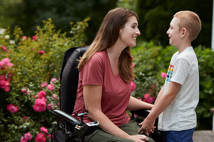 Femme assise dans un fauteuil roulant et souriant à un jeune garçon en extérieur